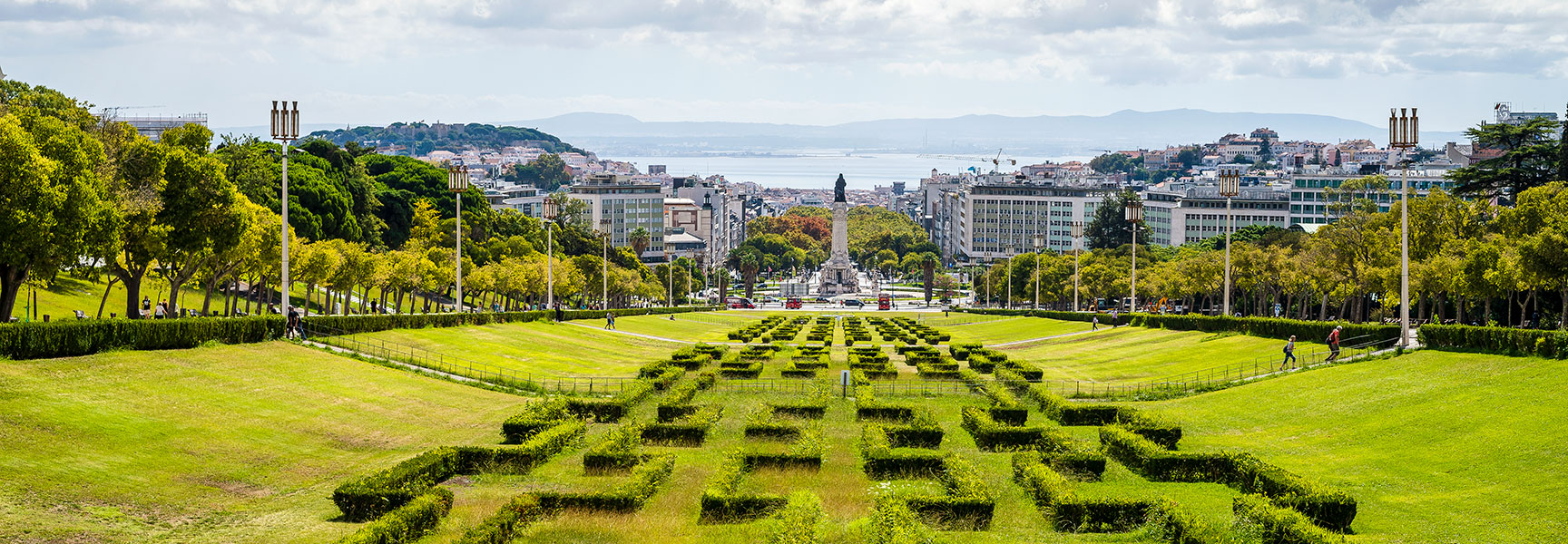 Manicured lawns and geometric hedges of Eduardo VII Park slope down towards the Marquis of Pombal Square and the city of Lisbon.