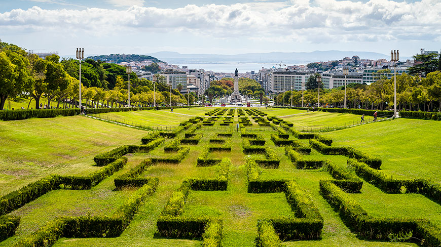 Looking down from Eduardo VII Park over a geometric hedge garden towards the Marquis de Pombal Square and the city of Lisbon beyond.