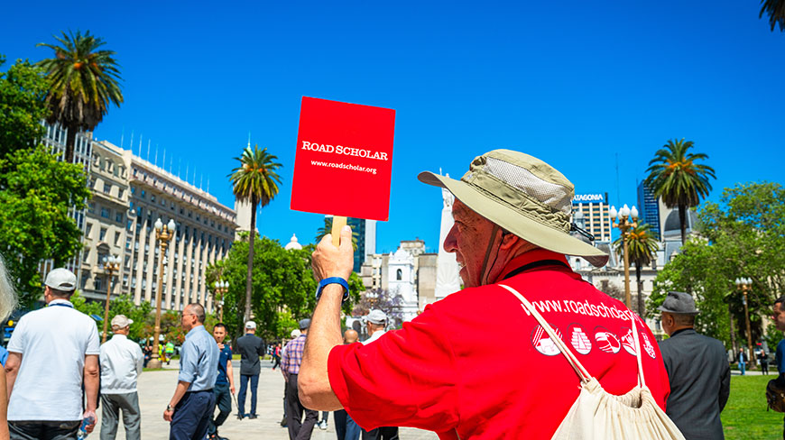 A Road Scholar tour guide in a red shirt holds up a sign while leading a group on a walking tour in Buenos Aires.