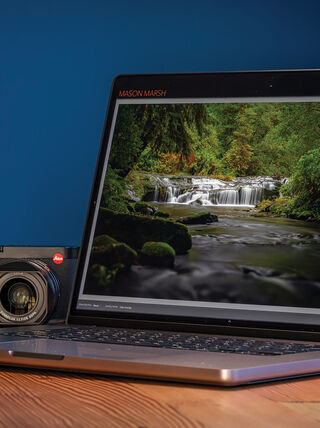 A laptop on a wooden desk displays Adobe Lightroom processing a waterfall landscape photo next to a camera, illustrating Mason Marsh's digital image workflow.