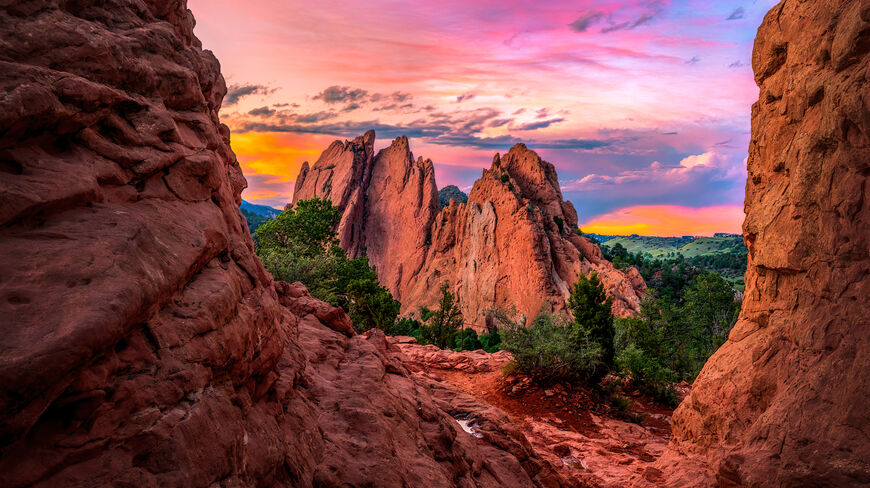 Vibrant pink and orange sunset sky over the towering red rock formations of Garden of the Gods in Colorado Springs, Colorado.