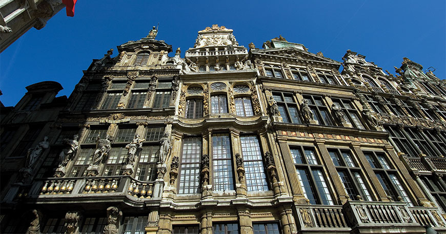 Ornate historic guildhall buildings with golden accents and statues under a clear blue sky at the Grand Place in Brussels.