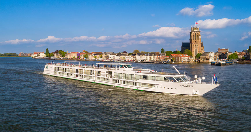 MS Lafayette river cruise ship sails on a wide river past a European waterfront town featuring a large historic church tower.