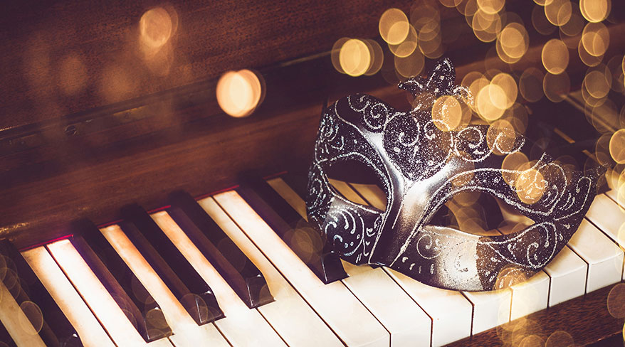 A black glittery Mardi Gras mask rests on the keys of a piano in New Orleans, surrounded by golden bokeh lights.
