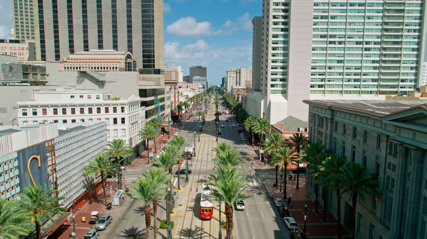 High-angle view of Canal Street in New Orleans featuring a red streetcar traveling through a palm tree-lined boulevard surrounded by tall city buildings.