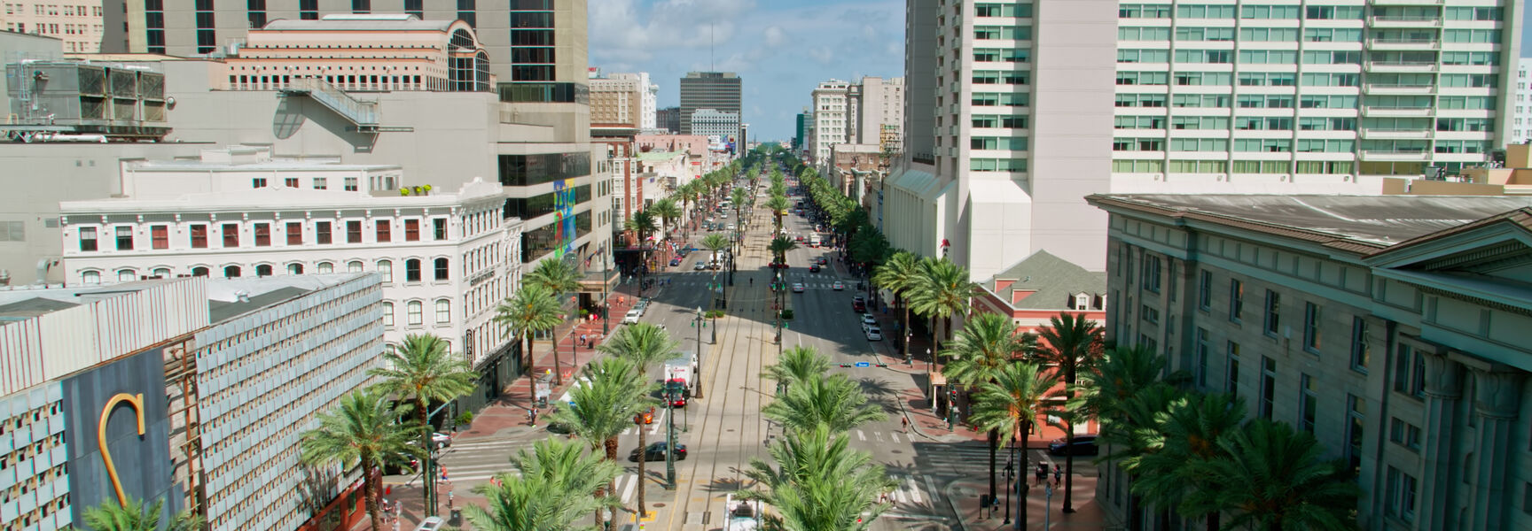 High-angle view of Canal Street in New Orleans featuring a red streetcar traveling through a palm tree-lined boulevard surrounded by tall city buildings.