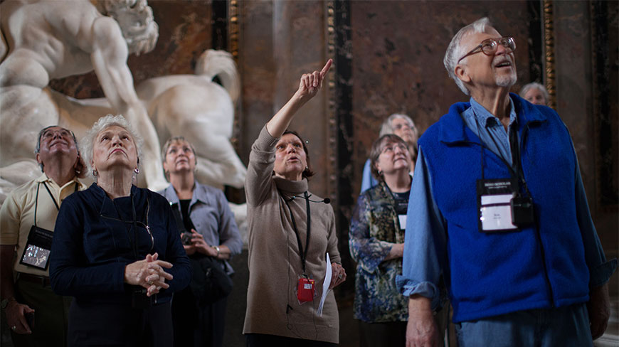 A group of tourists looks up while a guide points toward the ceiling inside the Kunsthistorisches Museum in Vienna.