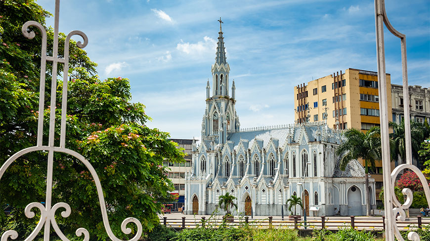 The Gothic-style La Ermita church in Cali, Colombia, framed by an ornate white gate under a bright blue sky.