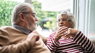 An older man and woman are sitting on a couch and having a serious conversation.