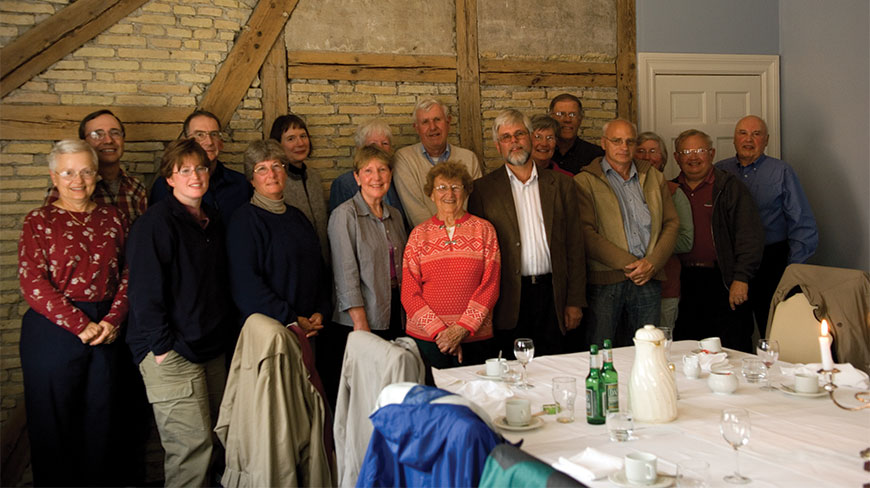 A group of people poses for a photo behind a set dining table in a Reykjavik room with rustic brick and wood walls.