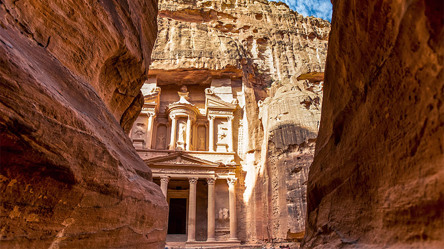 The ancient Treasury facade in Petra, Jordan, is framed by the towering sandstone walls of a narrow canyon.