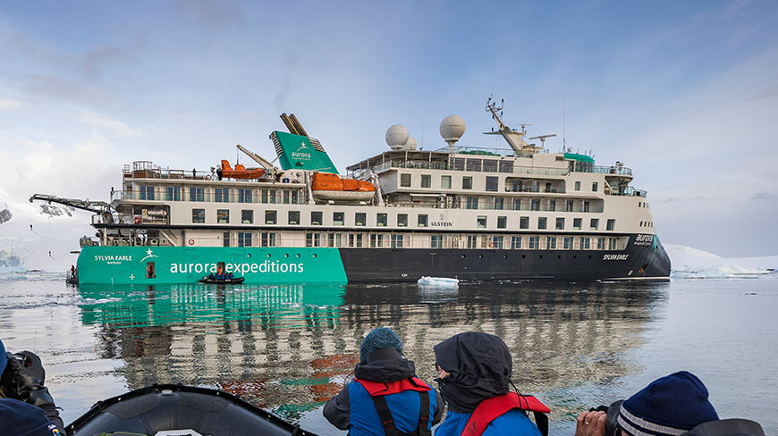 Passengers in a Zodiac boat go cruising past the Sylvia Earle ship near Prospect Point, Antarctica, surrounded by icy waters.