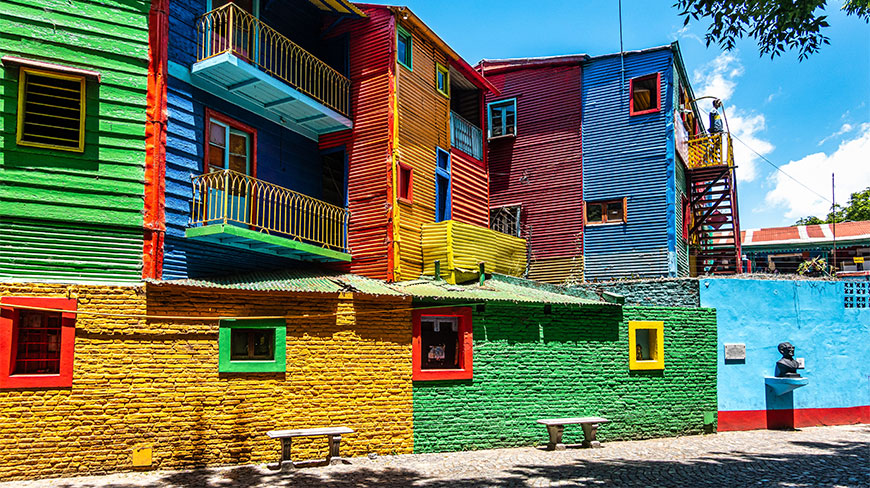 Brightly painted corrugated metal buildings in primary colors line a street in the La Boca neighborhood of Buenos Aires, Argentina.