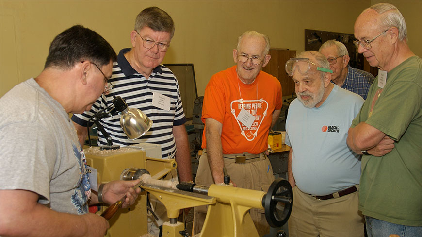 A group of men watches a woodworking demonstration on a lathe at Cedar Lakes in West Virginia.