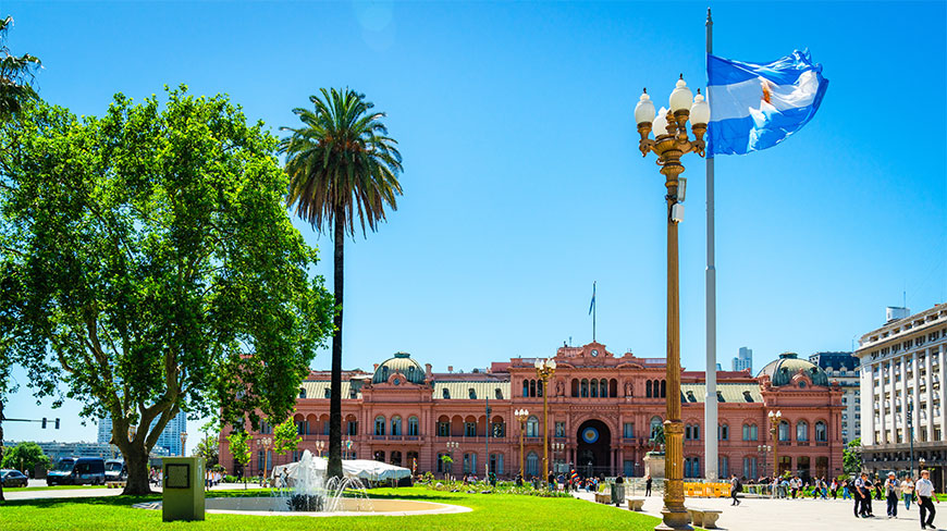A large Argentine flag flies near the Casa Rosada during a Buenos Aires downtown walking tour in a sunny public plaza.