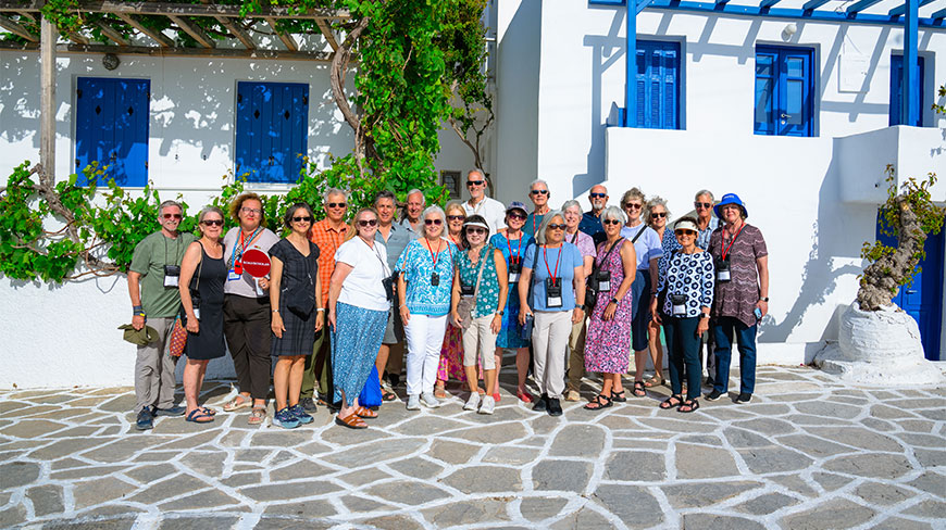 A group of tourists on a walking tour in Parikia, Paros, posing in front of traditional white buildings with bright blue shutters.
