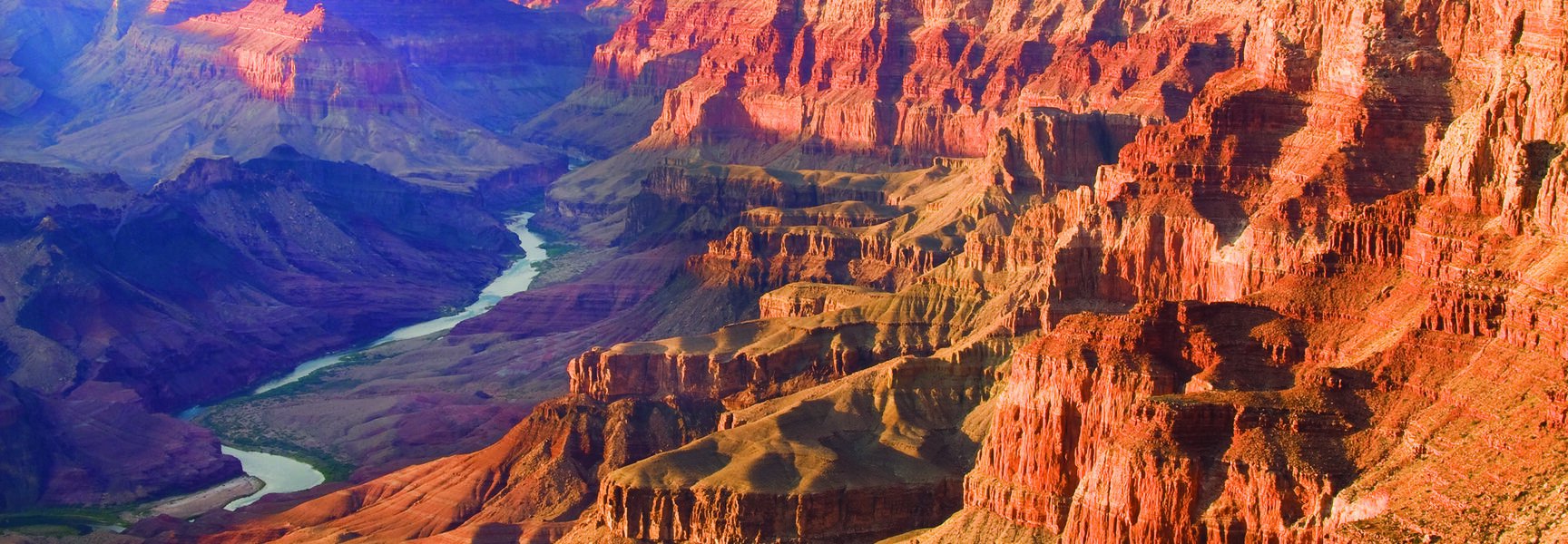 A bird’s-eye view of the Colorado River winding through the massive red rock formations of Grand Canyon National Park in Arizona.