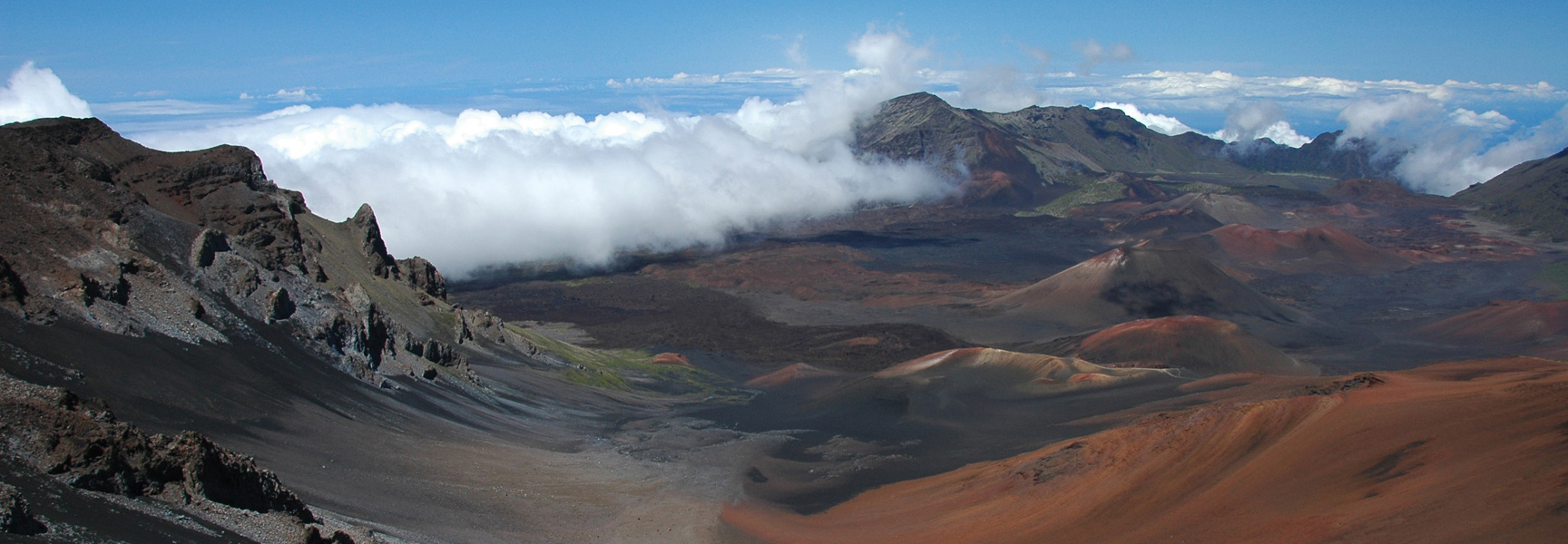 A wide view of a volcanic crater in a national park in Hawaii, with clouds rolling through the valley.