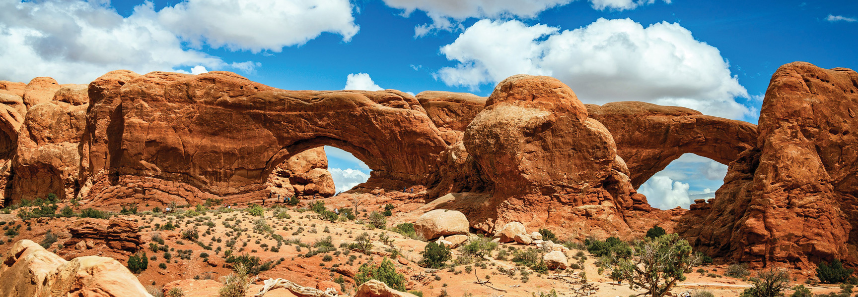 Massive red sandstone arches stand against a partly cloudy blue sky in the desert landscape of Utah.