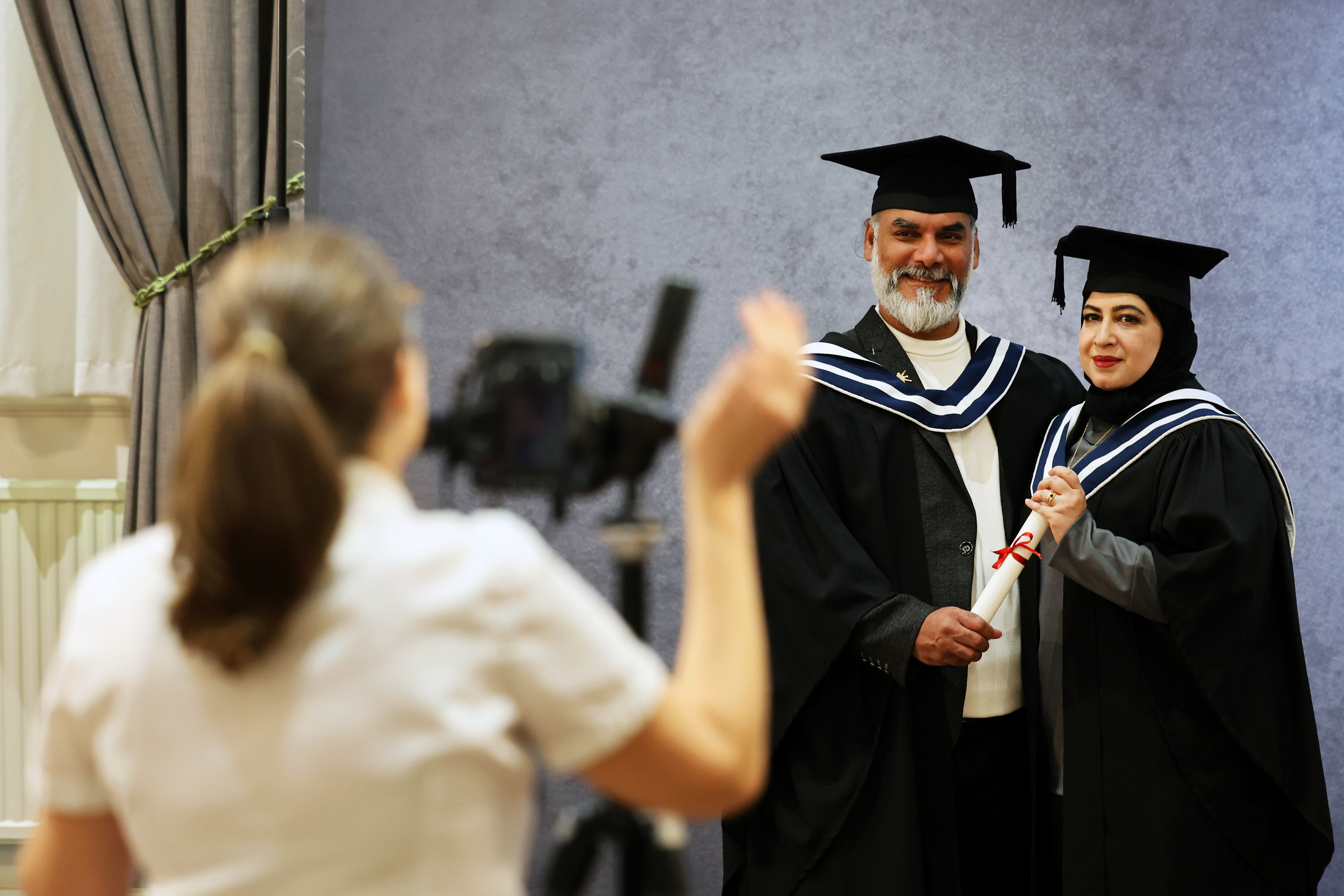 Photographer taking a picture of two graduates, male and female, who are standing side by side