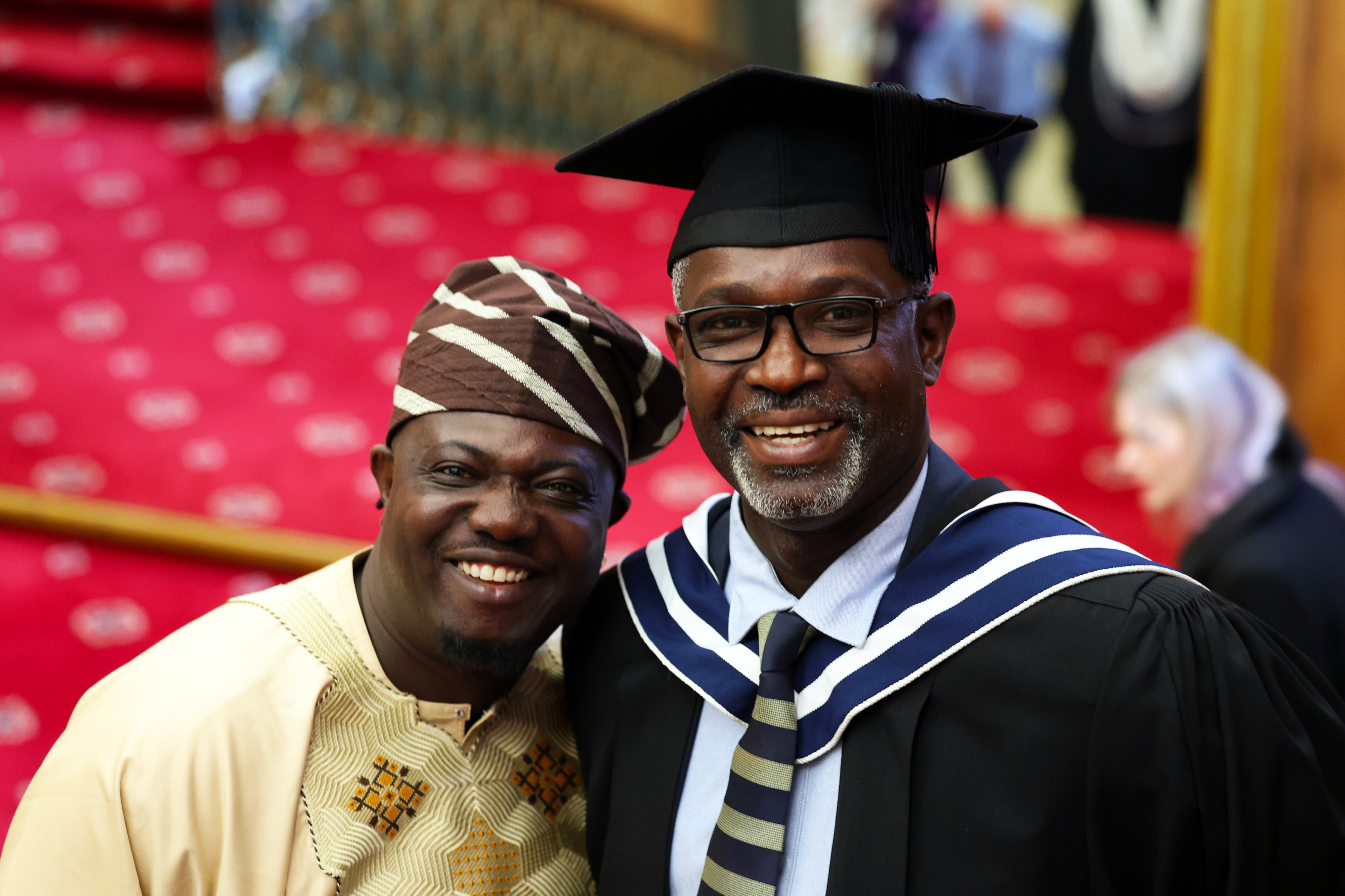 Male graduate in cap and gown posing with a loved one (husband or family member) after the ceremony