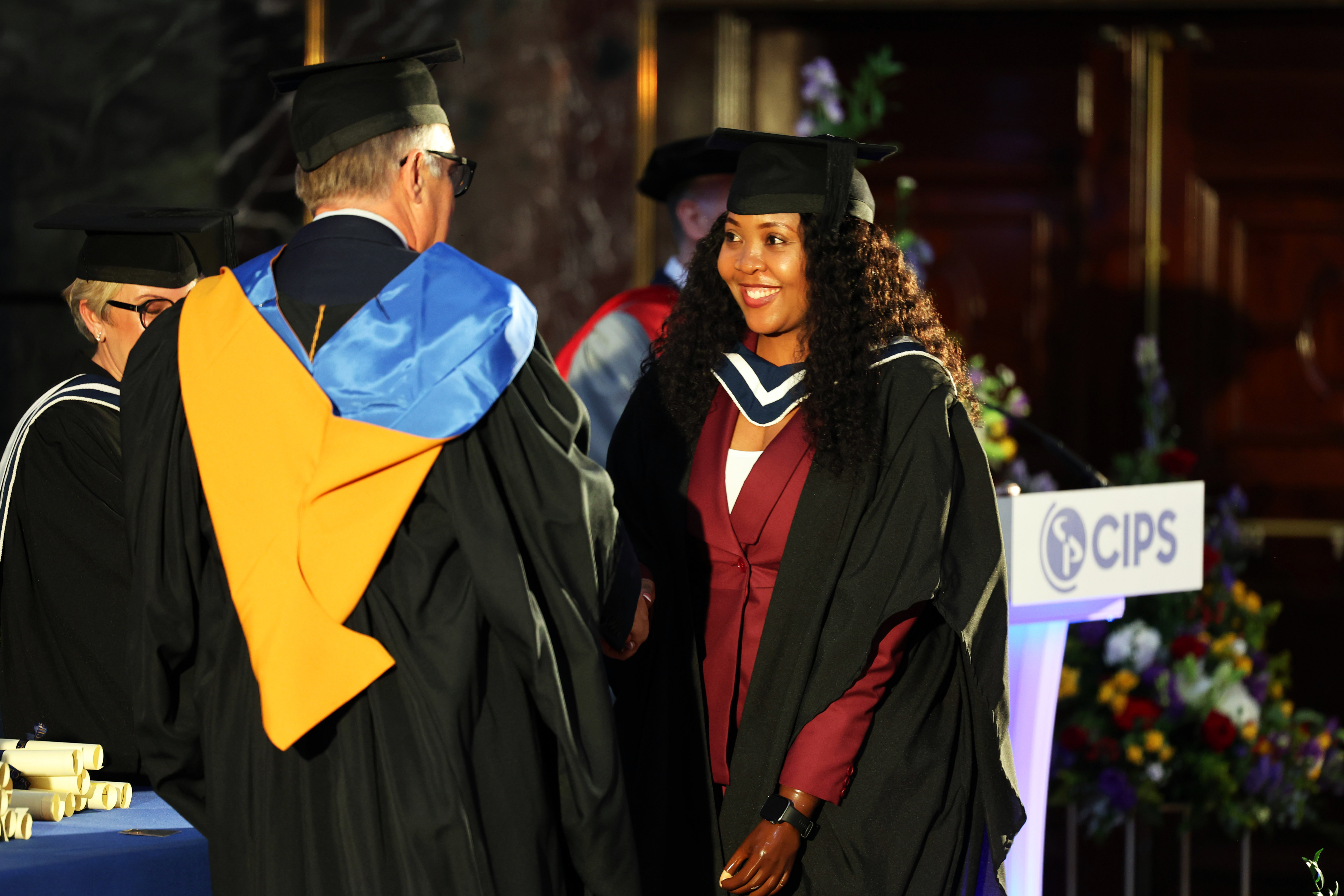 Female graduate in cap and gown on the stage shaking hands with CIPS CEO