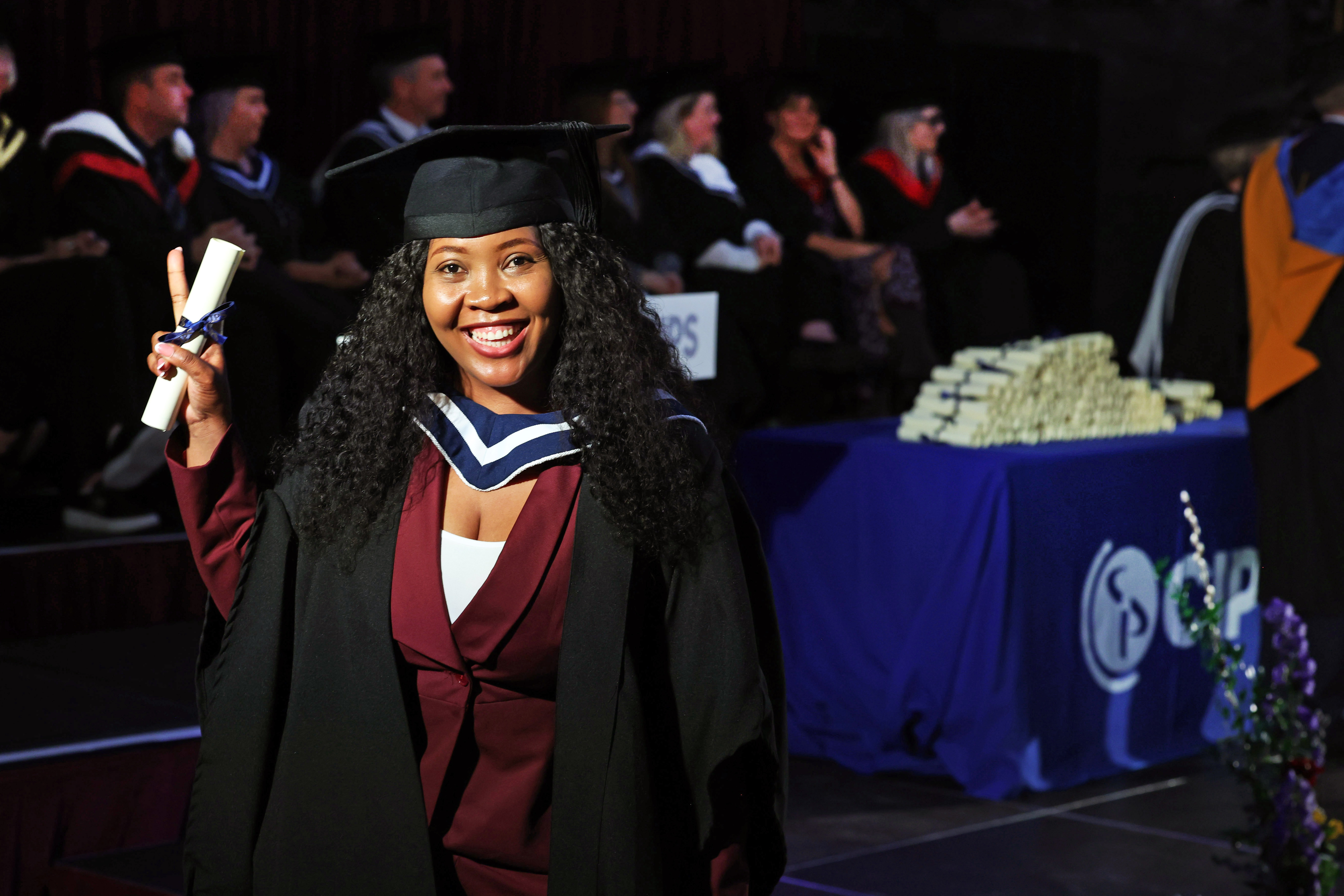Female graduate in cap and gown posing on stage holding her diploma