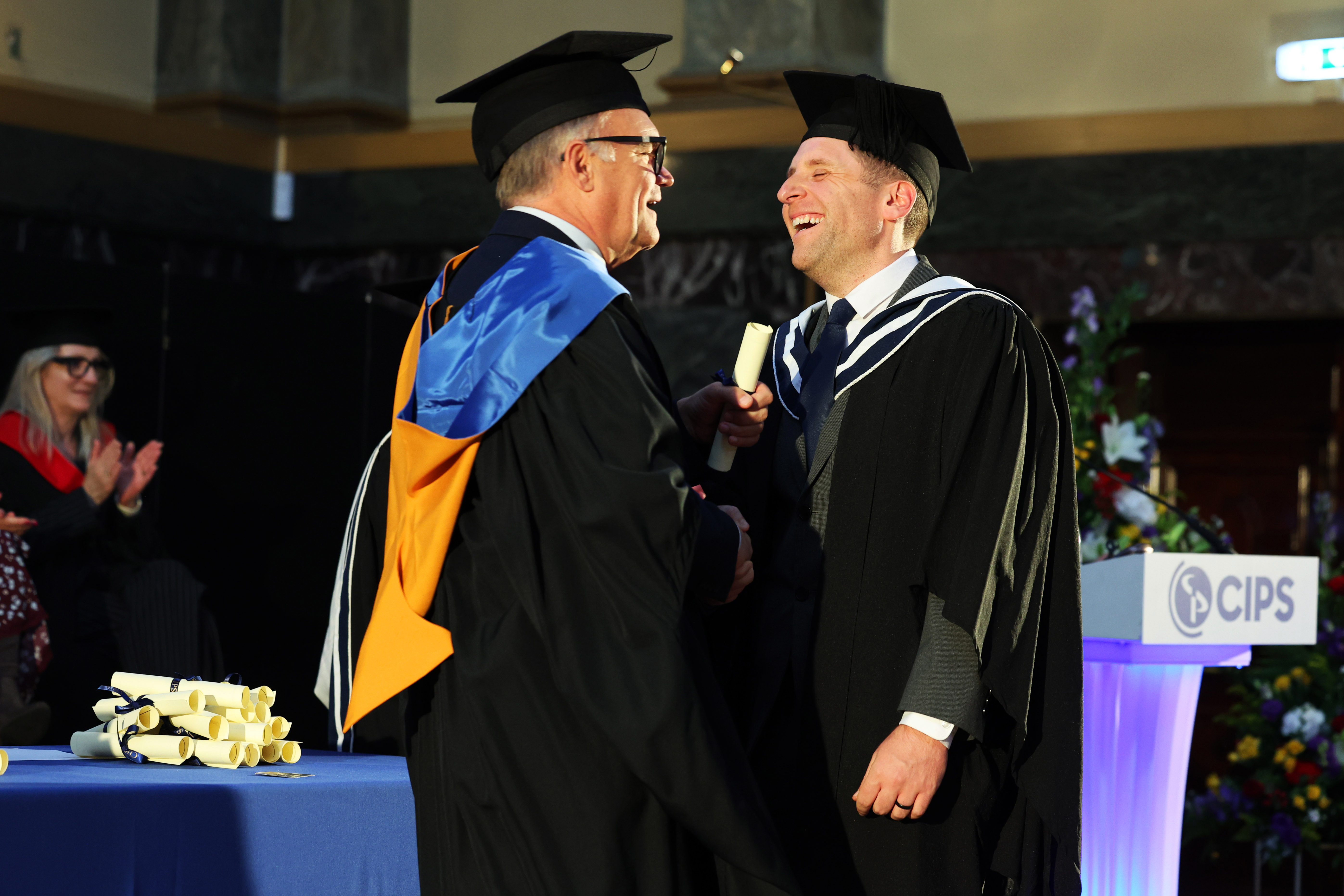Male graduate in cap and gown on the stage shaking hands with CIPS CEO