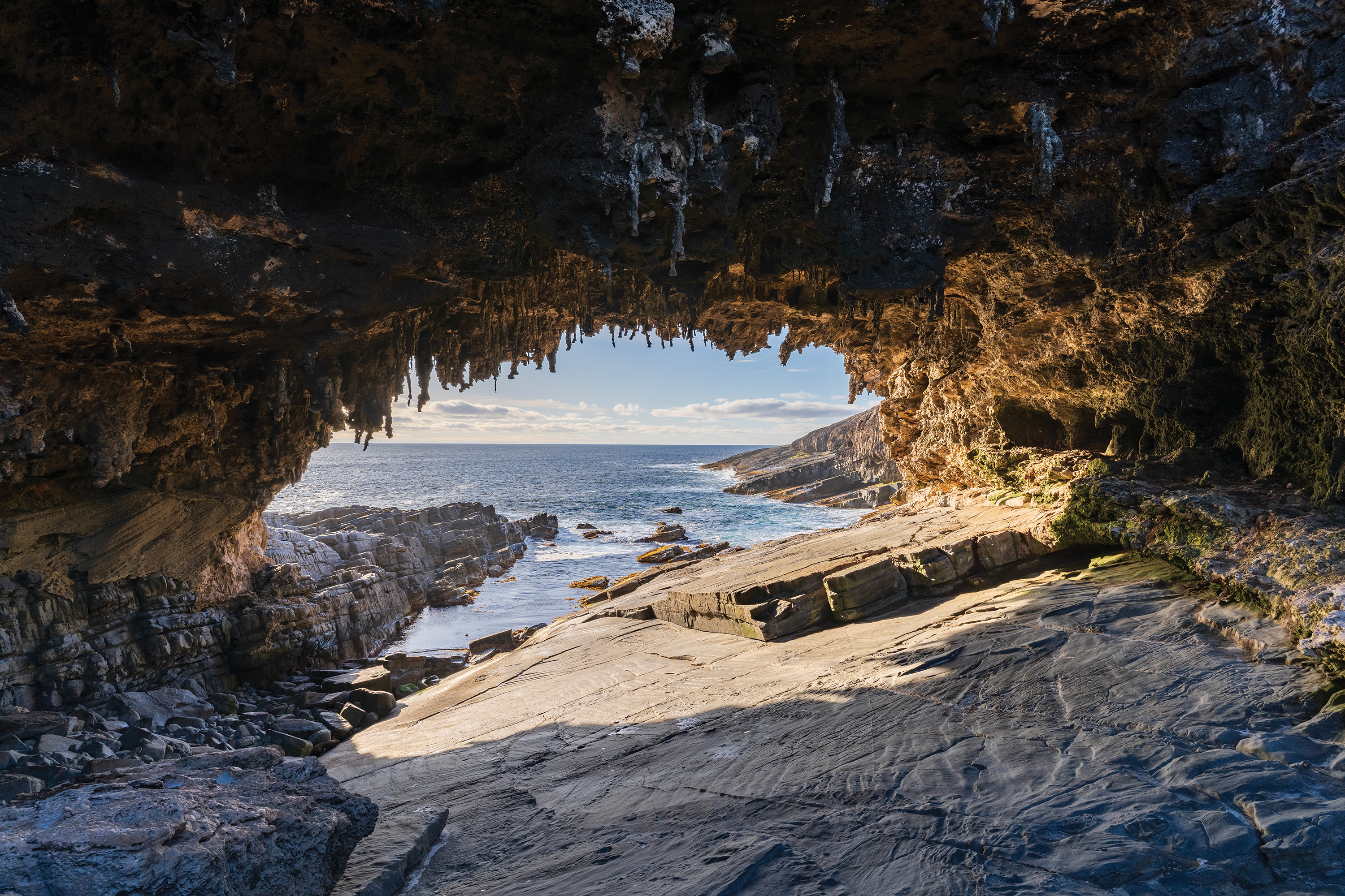 A view from inside a rocky coastal cave in Australia looking out towards the ocean, part of the Great Australian Train Trek landscape.