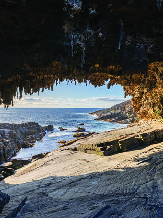 A view from inside a rocky coastal cave in Australia looking out towards the ocean, part of the Great Australian Train Trek landscape.