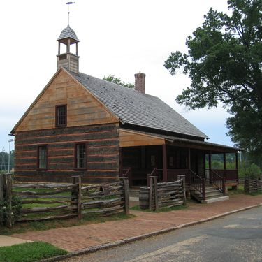The historic log-built St. Phillips Church in Salem, North Carolina, features a wooden cupola and a front porch, situated behind a split-rail fence.