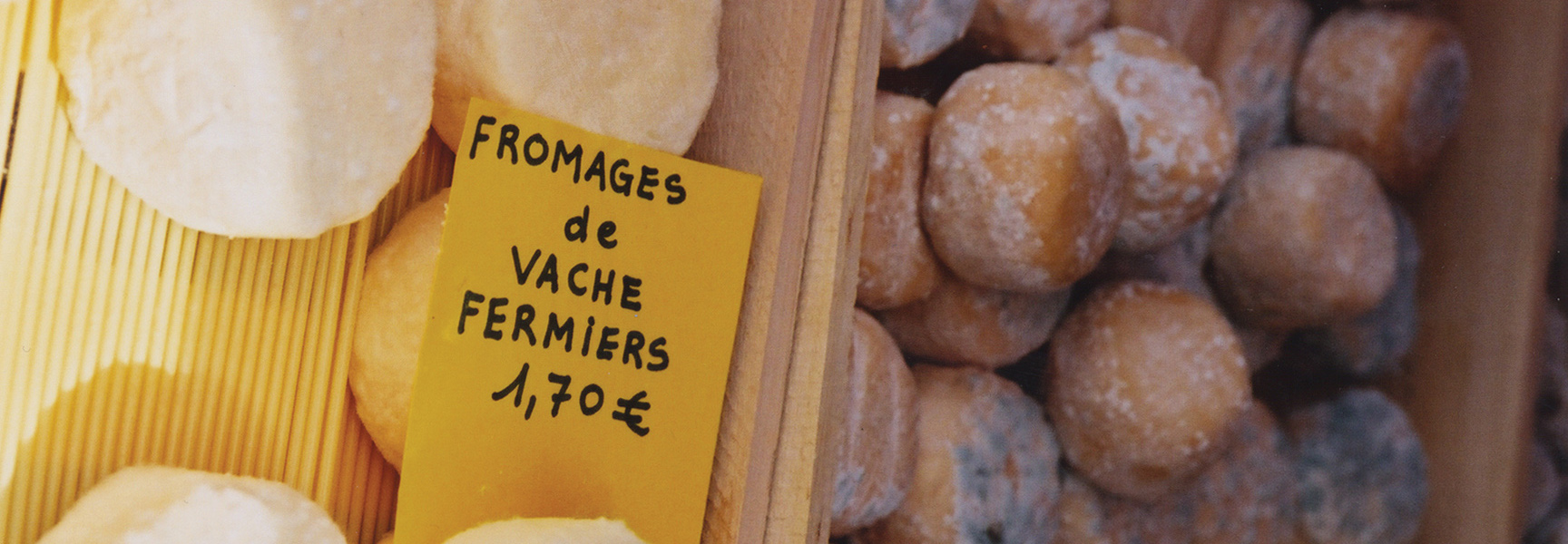 A yellow price tag sits next to wheels of fresh farmer's cheese at a local market in France.