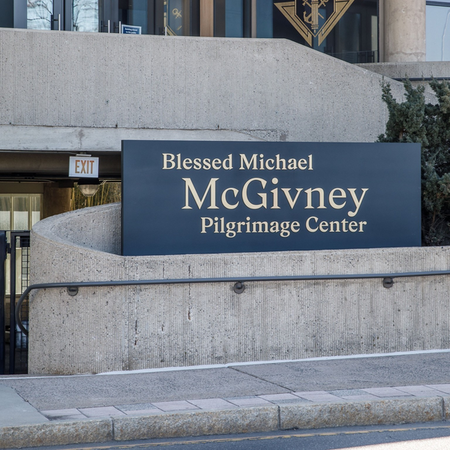 Black and gold Blessed Michael McGivney Pilgrimage Center signage on concrete exterior of building