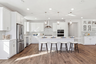 kitchen with white cabinets & counters, wood floors, three brushed nickel pendant lights above island with four espresso barstools