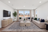great room with two tans sofas, patterned tan & blue area rug, light wood coffee table, and multiple windows