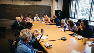 A small group of people sits around a large conference table, engaged in a lively discussion during a literature conference in California.