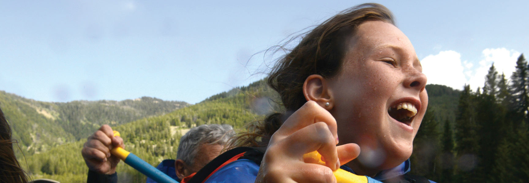 A young girl laughs with excitement while holding a paddle on a whitewater rafting trip in Idaho.