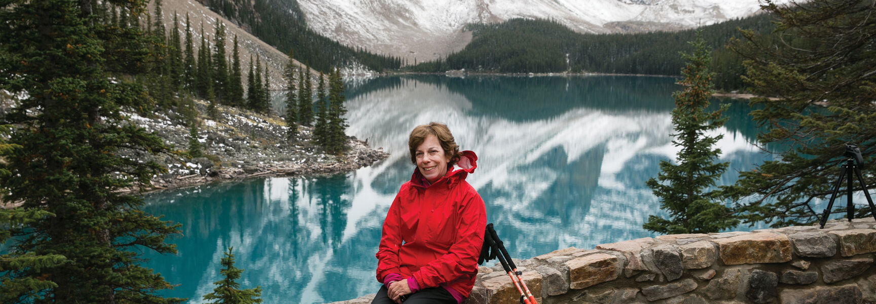 A hiker in a red jacket sits overlooking a turquoise alpine lake in the Canadian Rockies of Banff National Park, Alberta.