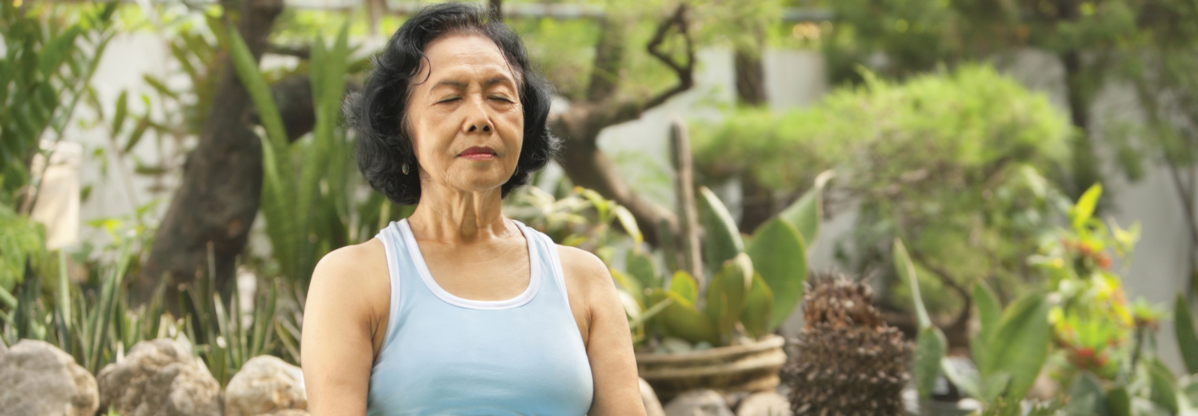 A woman meditates with her eyes closed in a lush, green garden during a rejuvenation retreat in California.