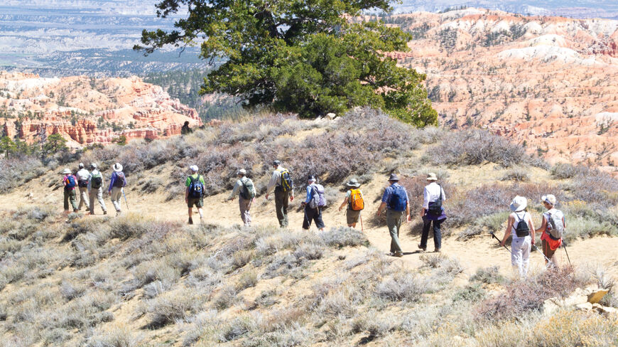 A group of hikers follows a trail overlooking the iconic red rock spires and hoodoos of Bryce National Park in Utah.
