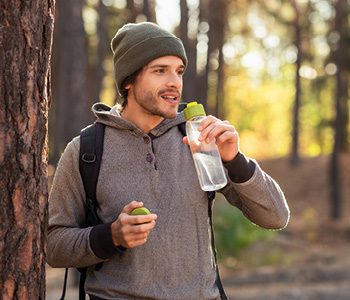 Zdrav življenjski slog je odličen način za krepitev imunskega sistema, mlad moški zato uživa požirek čiste vode na sprehodu v naravi.