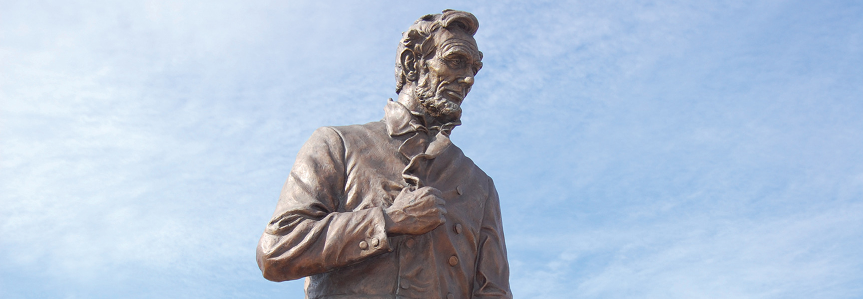 A bronze statue of Abraham Lincoln in Illinois looks thoughtfully downwards against a pale blue sky.