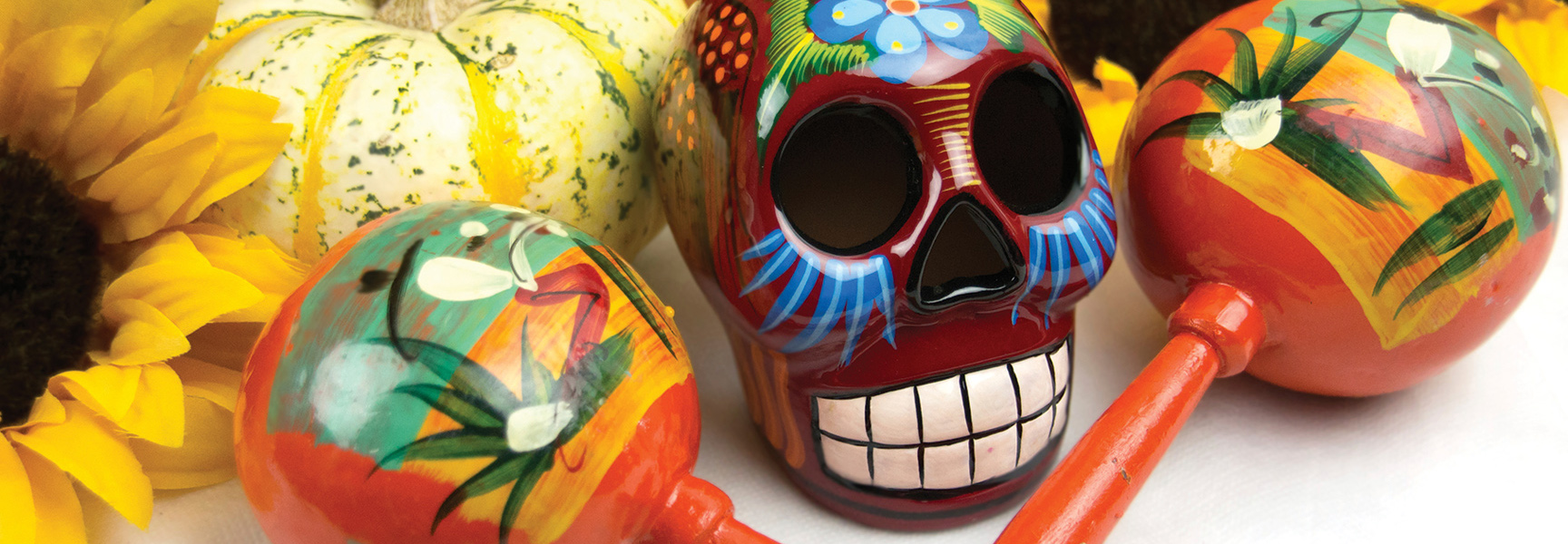 A brightly painted sugar skull, maracas, and sunflowers arranged for a Día de Los Muertos celebration in Mexico.
