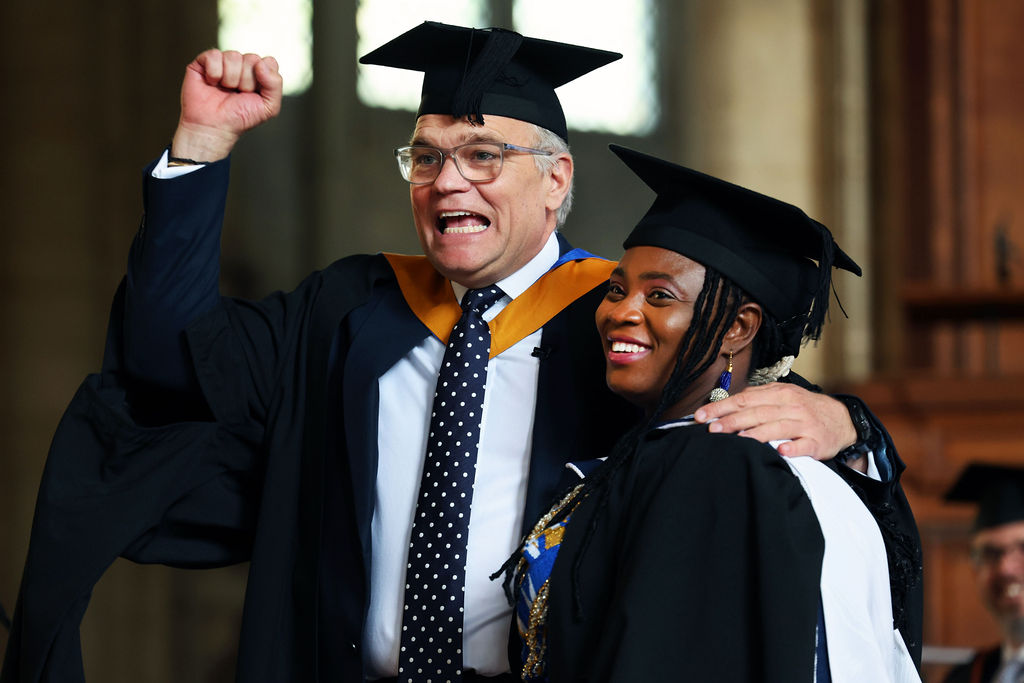 A graduate in academic dress is cheered on by another man