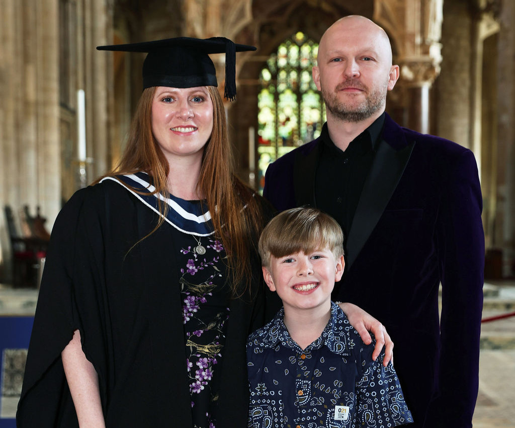 A woman in a cap and gown poses with a man in a purple jacket and a young boy in a patterned shirt