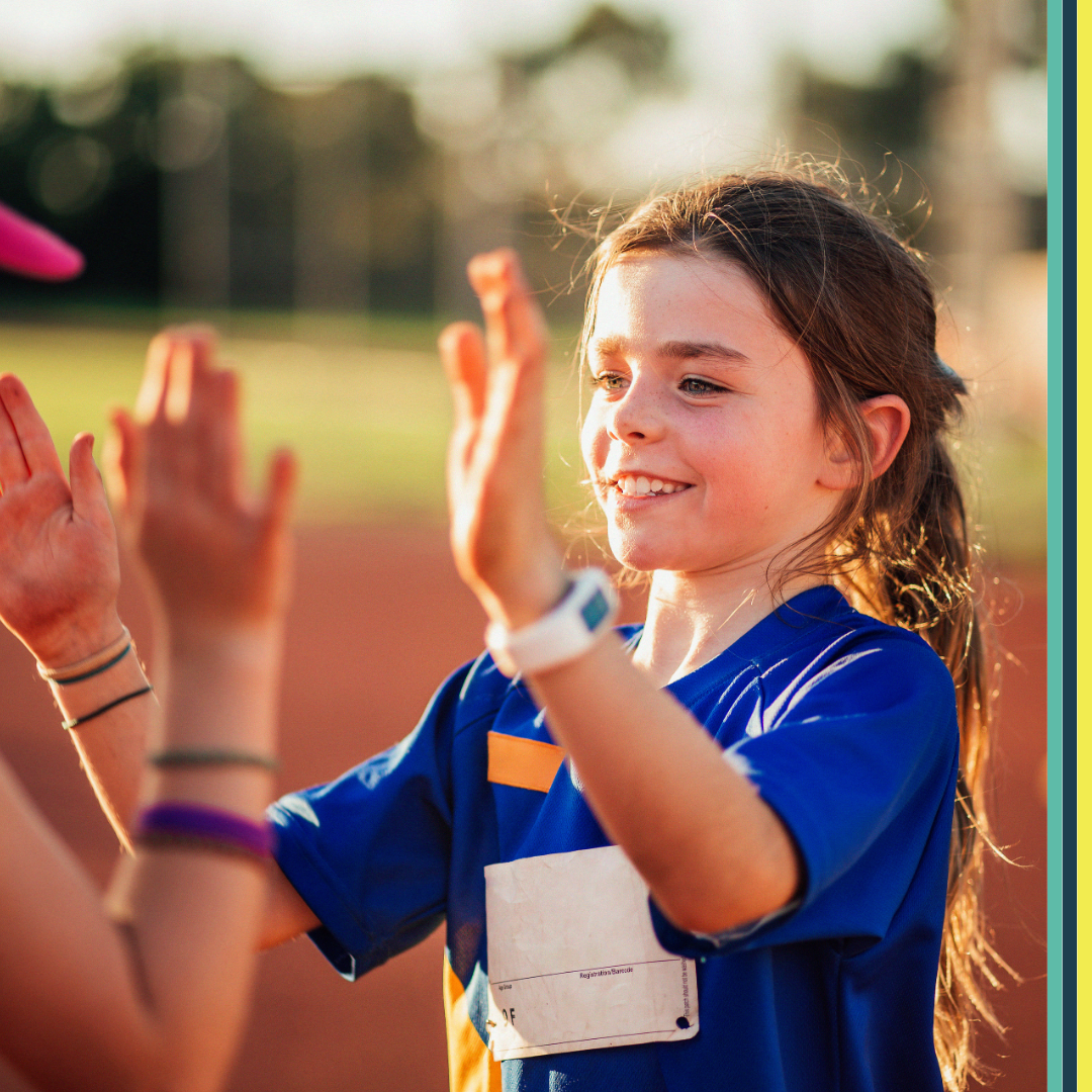 A young girl giving a high five at a athletics track with her friend smiling