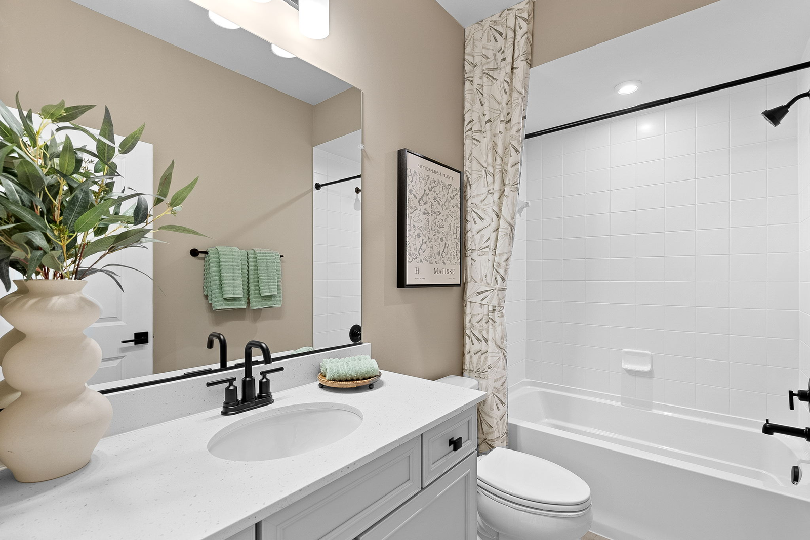 bathroom with white sink, black hardware, toilet, and tub and shower with white tile