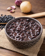 Cooked black beans in a bowl over wooden table with onion and garlic.