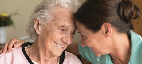 A caregiver and senior adult woman sharing a smile together