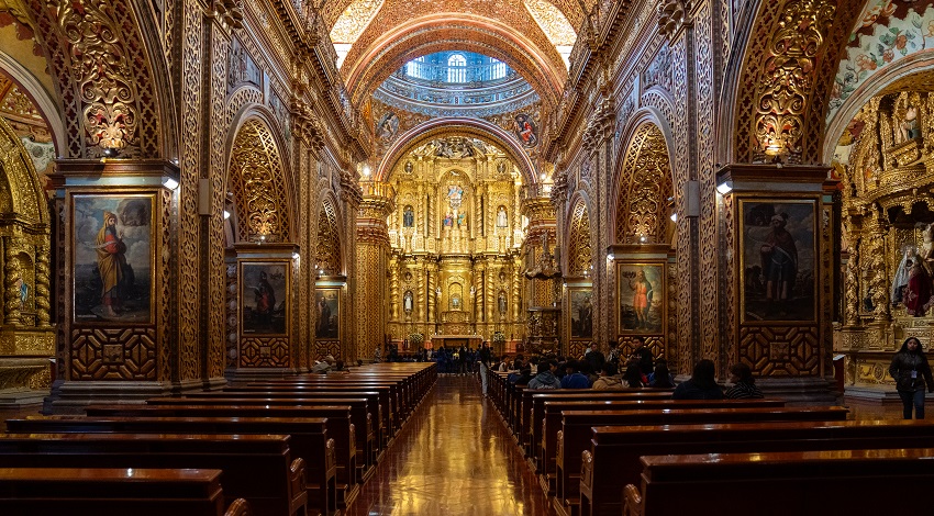 An aisle stretches down the center of a church with gold covering its walls and arches